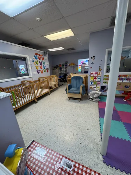 Infant room view with cribs along the wall, a rocking chair, and soft colorful floor mats