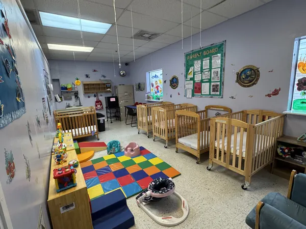 Infant room with rows of wooden cribs and a bright foam mat