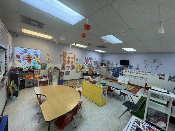 Bright preschool classroom with child-size tables, learning centers, and colorful wall art