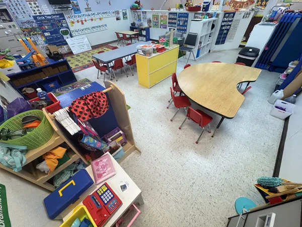 Preschool classroom with kidney-shaped tables, red chairs, and a play kitchen