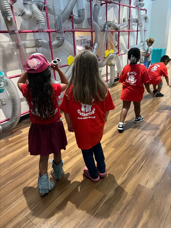 Summer campers in matching red shirts exploring a hands-on ball exhibit at a children's museum