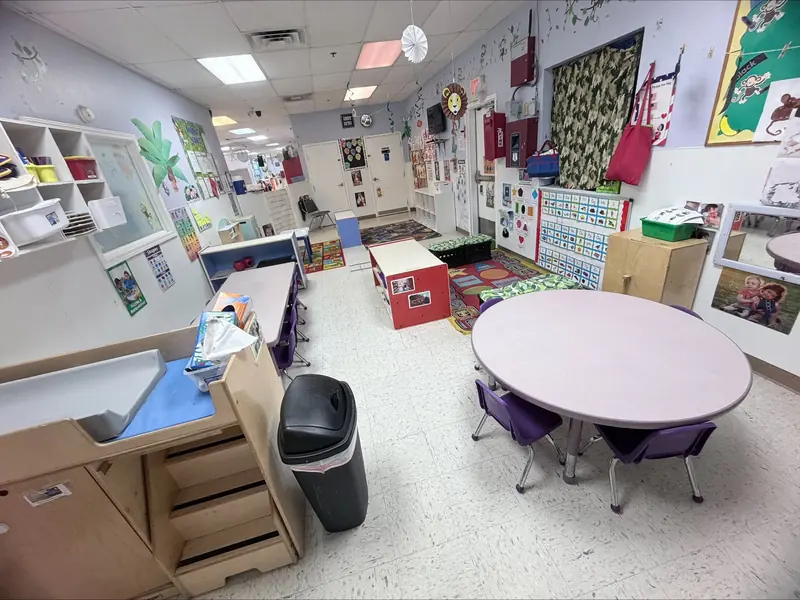 Toddler classroom with a round table, small purple chairs, and cubbies