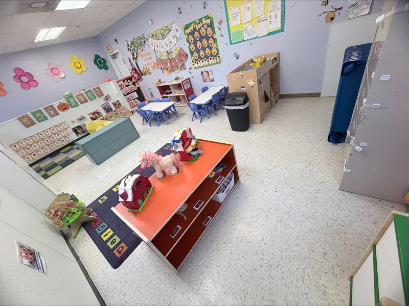Toddler classroom with a red play table, toy shelves, and colorful wall art